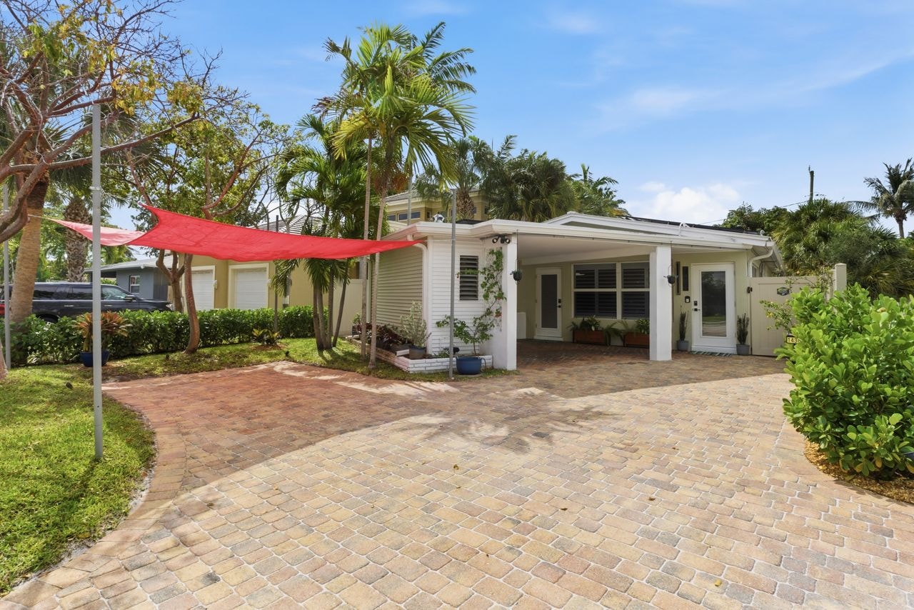 Front exterior with paver driveway, red shade sail, and lush tropical landscaping