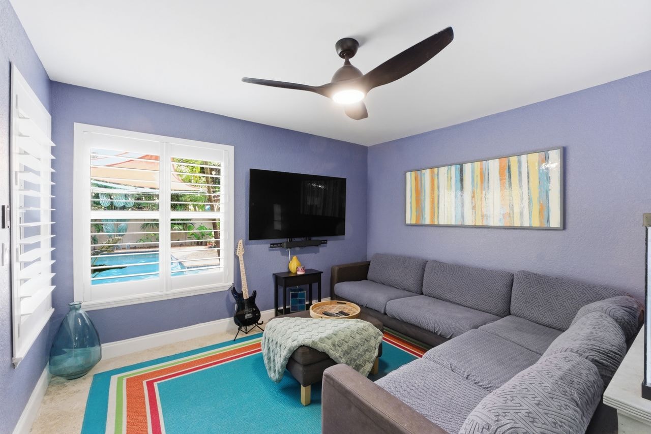 Living room with sectional sofa, large TV, and pool views through plantation shutters
